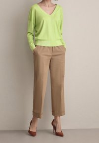 Maglione verde lime con scollo a V e texture a coste, abbinato a pantaloni leggeri marroni su misura e scarpe con tacco alte marroni.