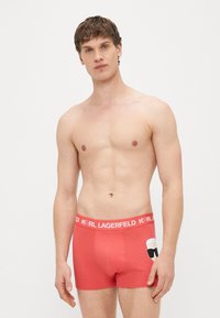 Boxer rouge pour hommes avec une ceinture �élastique portant la marque "KARL LAGERFELD" et un motif de lunettes de soleil sur le côté.