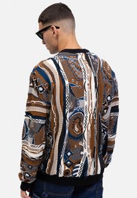 Gestreifter Pullover mit komplexen Designs in Braun, Blau und Weiß, mit gerippten schwarzen Bündchen und Saum sowie einer lockeren Passform.