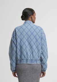 Zila, kviltota bumbiera jakas ar dimanta rakstu, elastīgām aprocēm un apakšmalu. Mīksta tekstūra, apaļš kakls un brīva piegriezuma dizains.