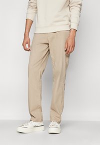Pantaloni beige realizzati in tessuto morbido, con design a gamba dritta, vita piatta e una texture sottile. Abbinati a sneakers casual bianche.