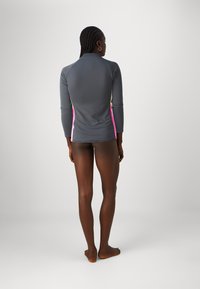 Sivi rash guard dugih rukava s ružičastim i žutim bočnim akcentima. Glatki, rastezljivi materijal. Ima visok ovratnik za dodatnu zaštitu.