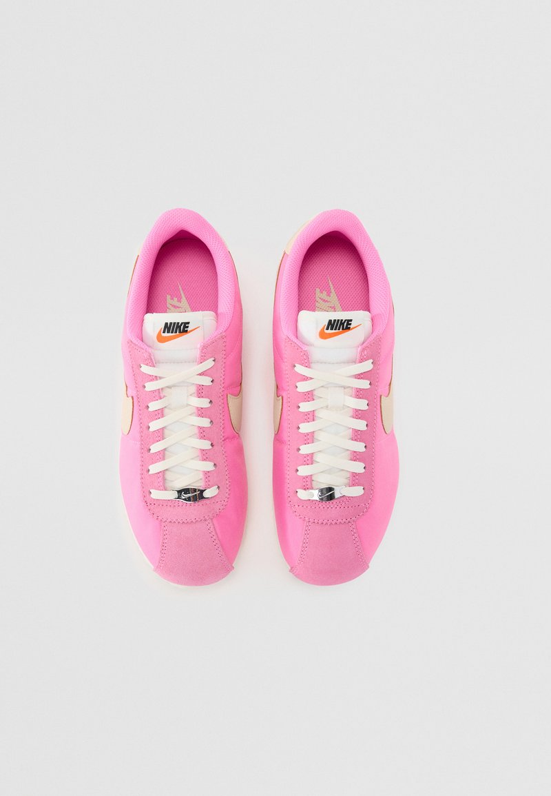 Rosa Nike Sneaker mit Obermaterial aus Wildleder und Stoff, ausgestattet mit weißen Schnürsenkeln, einem cremfarbenen Seiten-Swoosh und einem markenbezogenen Zungen-Label.