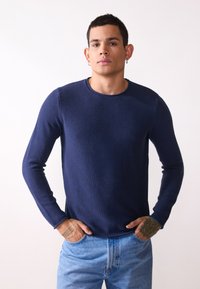 Marine crew-neck genser med lange ermer, teksturert strikkemønster, ribbede kanter, parret med lyseblå jeans. Tett passform med splitt på sidene.