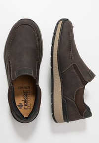 Braune Leder Slipper mit kontrastierender beige Gummisohle, dekorativer Naht und einem strukturierten Seitenpaneel für einfaches An- und Ausziehen.