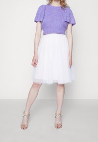 Paars gebreid crop top met korte mouwen, witte tule knie-lange rok met sprankels, en beige strap-sandaletten met een hak. Eenvoudige en elegante outfit.