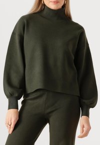Donkergroene coltrui met een losse pasvorm, verlaagde schouders en lange, licht opgeblazen mouwen. Zachte gebreide textuur, cropped zoom.