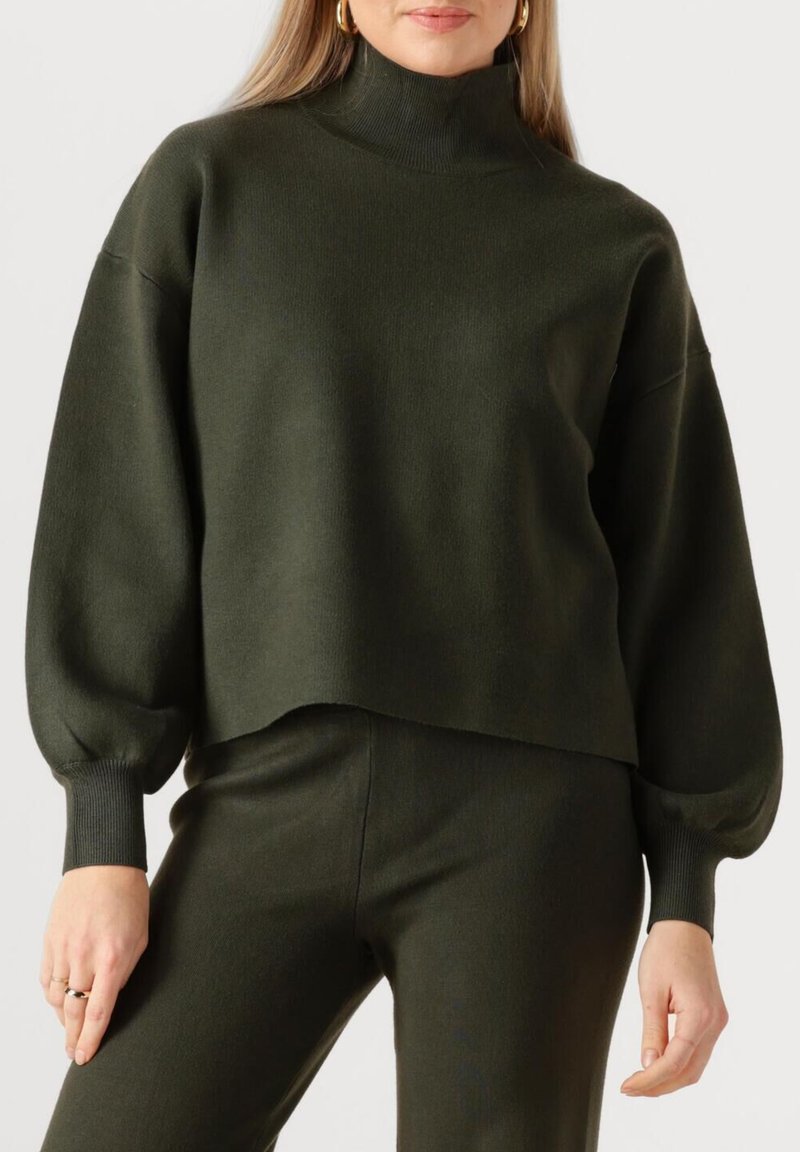 Donkergroene coltrui met een losse pasvorm, verlaagde schouders en lange, licht opgeblazen mouwen. Zachte gebreide textuur, cropped zoom.
