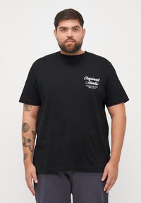 Schwarzes T-Shirt mit kurzen Ärmeln aus Baumwolle und Rundhalsausschnitt. Mit weißem Textlogo auf der linken Brustseite. Einfacher, lässiger Schnitt.