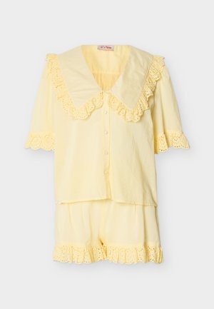 Κίτρινο σετ πιτζάμας με κοντά μανίκια, μεγάλο γιακά με βολάν, μπλούζα με κουμπιά μπροστά και ταιριαστό σορτς με διακοσμητικά βολάν από δαντέλα με τρύπες.