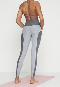 Šedé a světle šedé legíny s vysokým pasem, kontrastní boční panely a hladká textura. Úzký střih.
