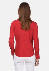 Rode lange mouw shirt met een gladde textuur, aansluitend design en knoopmanchetten. De achterkant toont een gebogen zoom en naaddetails.