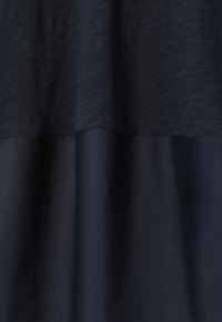 Tissu bleu marine foncé avec un design bicolore subtil présentant des textures et des sections lisses, suspendu avec de doux plis.