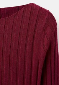 Gros plan sur un tissu en tricot côtelé bordeaux d'un vêtement à manches longues avec des rayures texturées verticales.