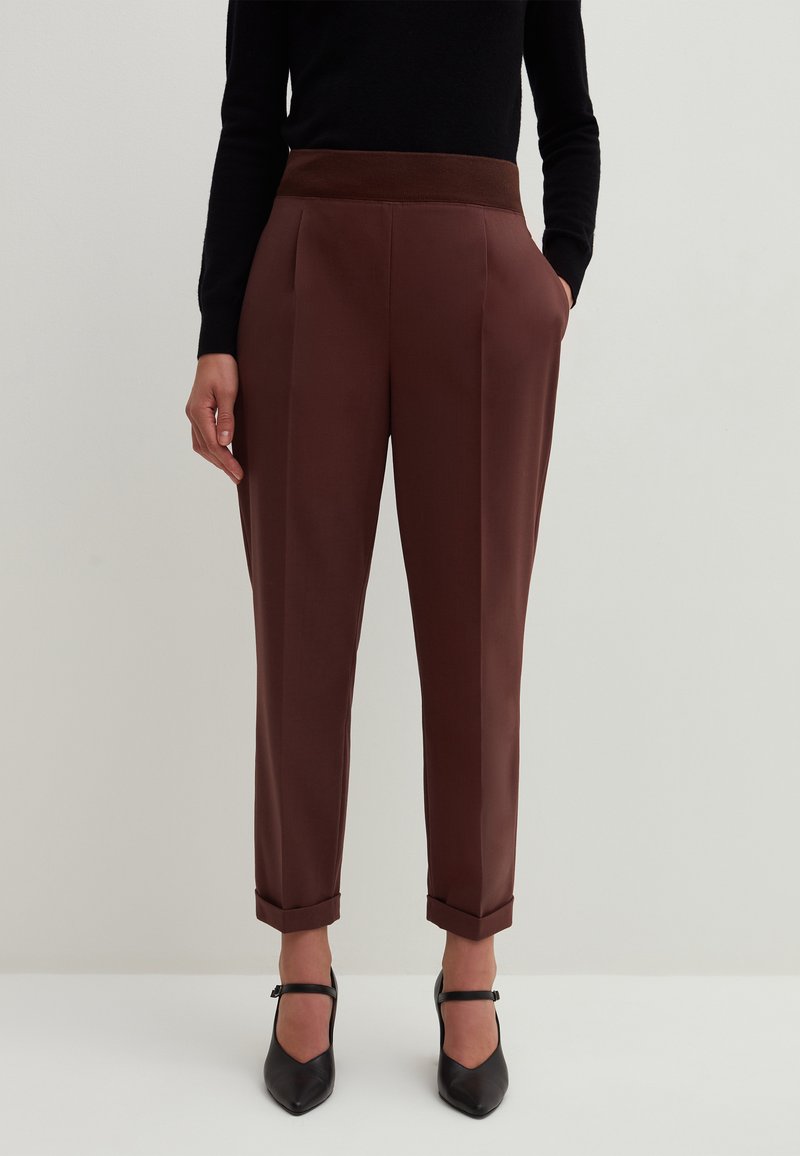 Braune maßgeschneiderte Hosen mit einem gerippten elastischen Bund, hochgerollten Säumen und Seitentaschen, kombiniert mit schwarzen spitzen Schuhen.