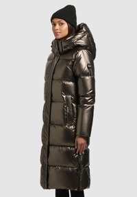 Fémes sötétbarna steppelt télikabát kapucnival, oldalsó cipzáras zsebekkel és térd hosszúságú, steppelt textúrával.