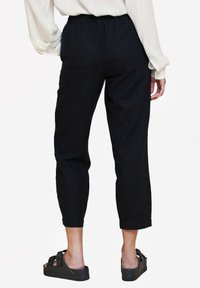 Černé zkrácené kalhoty s elastickým pasem, hladkým povrchem a ohrnutými lemy, doplněné černými sandály se sponou.