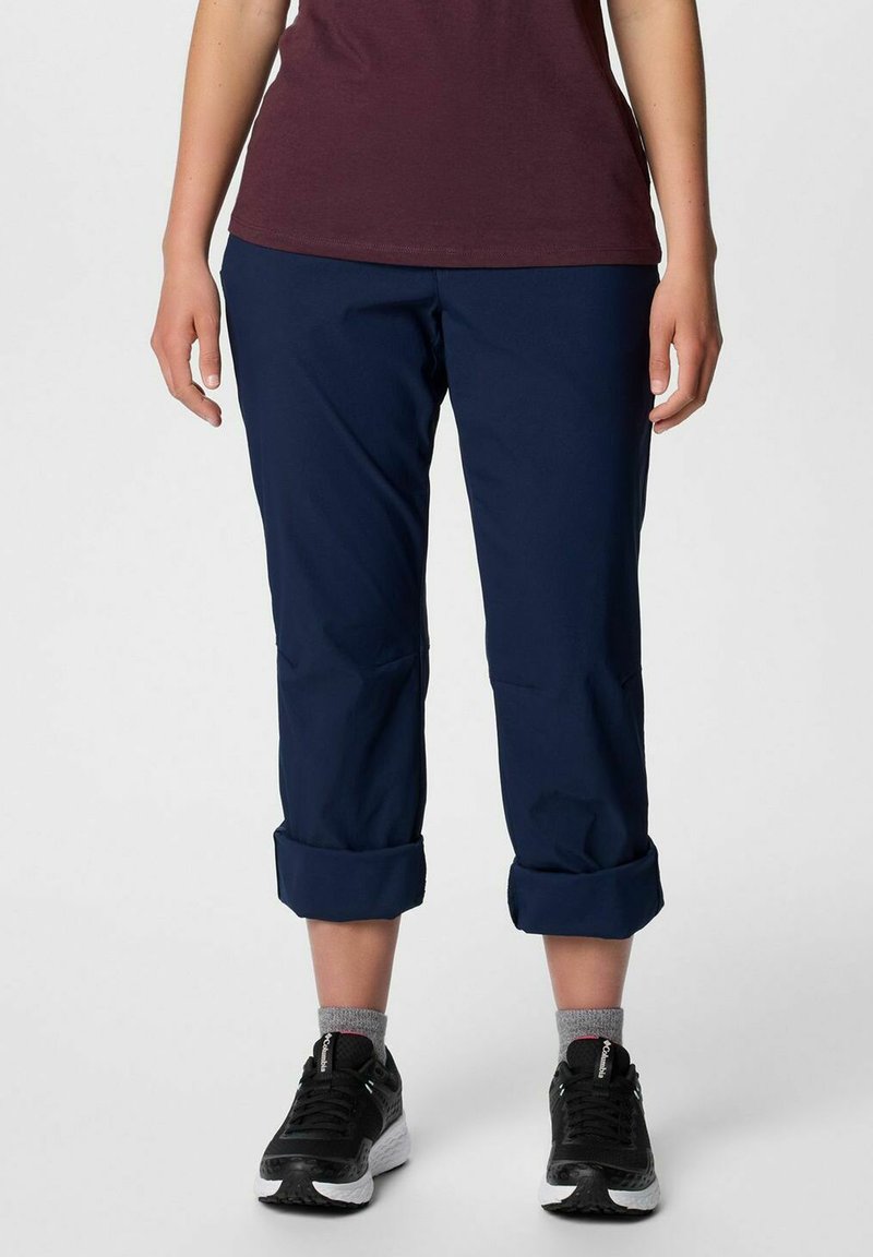 Granatowe, krótkie spodnie uszyte z lekkiego materiału, z podwiniętymi mankietami i prostym krojem nogawek. W połączeniu z czarno-białymi butami sportowymi.