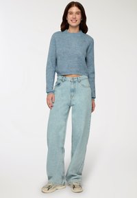 Przycięty niebieski sweter dzianinowy o prążkowanej strukturze, w połączeniu z jasnoniebieskimi dżinsami o szerokich nogawkach. Sneakersy w jasnym kolorze z ciemnymi akcentami.