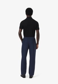 Camisa polo negra y pantalones azul marino de corte relajado, con cintura elástica y dos bolsillos traseros, vistos desde atrás.