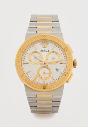 Versace kronográf karóra arany tónusú lünettával, fehér számlappal arany díszítésekkel, rozsdamentes acél szíjjal és bonyolult görög kulcs mintával.