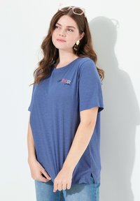 Niebieska koszulka z krótkim rękawem o luźnym kroju, z logo na przedniej kieszeni w czerwonym i czarnym kolorze. Wykonana z lekkiego, miękkiego materiału.