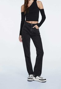 Top corto negro con un corte en un hombro, combinado con unos jeans negros de pierna recta de tiro alto y zapatillas blancas con acentos negros.