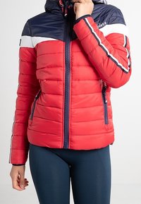 Rød dunjakke med navyblåt hætte og øverste sektion. Har hvide og navyblå striber på ærmerne, lynlås foran og to sidelommer.