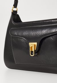 Borsa nera in pelle testurizzata. Presenta una chiusura in tonalità oro e una tasca frontale. Finitura liscia con bordi arrotondati e cuciture a contrasto.