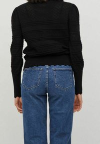 Zwarte gebreide trui met gestructureerde patronen, gecombineerd met blauwe hoge taille denim jeans met twee achterzakken en een lichte wassing.