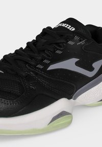 Μαύρο αθλητικό παπούτσι με λευκές και γκρι λεπτομέρειες, λογότυπο "Joma" στη γλώσσα, υφή στη σόλα και κείμενο "Perfect Fit" κοντά στα κορδόνια.