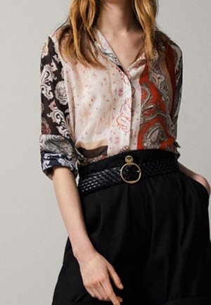 Bunt gemusterte Bluse mit Knopfdesign und aufgerollten Ärmeln, kombiniert mit hochgeschnittenen schwarzen Shorts und einem geflochtenen Gürtel mit einer runden Schnalle.