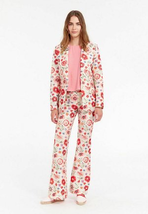 Costume à motifs floraux sur fond crème, avec des fleurs rouges et bleues. Pantalons évasés assortis et un haut rose doux.