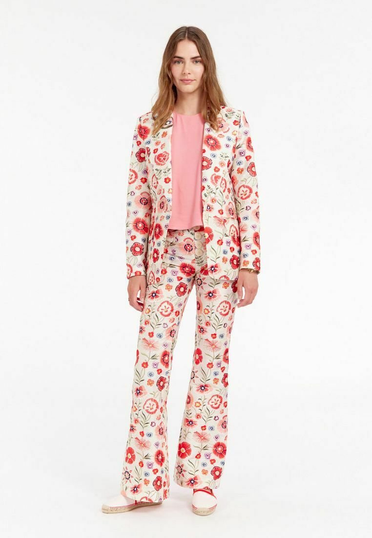 Costume à motifs floraux sur fond crème, avec des fleurs rouges et bleues. Pantalons évasés assortis et un haut rose doux.