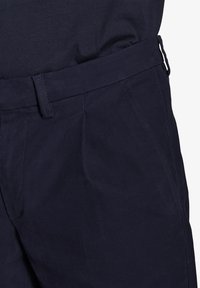 Pantaloni blu navy realizzati in tessuto testurizzato, con design a vita piana, tasche laterali e passanti per cintura in vita.