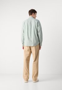 Camicia a righe verde chiaro e bianco con colletto button-down, abbinata a pantaloni beige e sneakers bianche, vista da dietro.