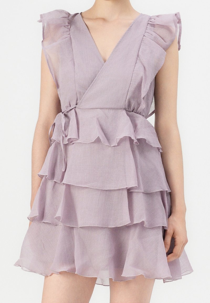 Robe en lavande avec volants, col en V, tissu transparent et couches superposées. Comprend des manches courtes flottantes et une ceinture à nouer à la taille pour ajustement.