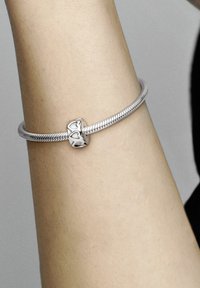 Silberarmband mit einer strukturierten Schlangenkette und einem zentralen Element mit Herz-Ausschnitten, getragen an einem Arm mit heller Hautfarbe.