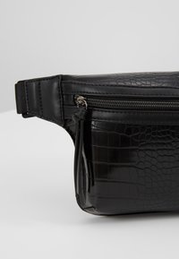 Banane noire en similicuir avec texture crocodile, poche avant zippée et sangle ajustable avec boucle.
