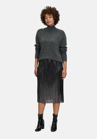 Grauer gestrickter Rollkragenpullover mit gerippten Bündchen, kombiniert mit einem schwarzen plissierten Midirock und glänzenden schwarzen Knöchelstiefeln.