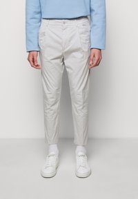 Pantaloni grigio chiaro con una vestibilità leggermente affusolata, realizzati in tessuto leggero. Dotati di tasche laterali e design a vita piatta. Abbinati a sneaker bianche.