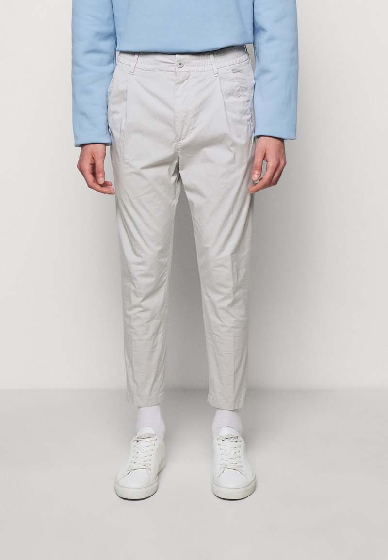 Pantaloni grigio chiaro con una vestibilità leggermente affusolata, realizzati in tessuto leggero. Dotati di tasche laterali e design a vita piatta. Abbinati a sneaker bianche.