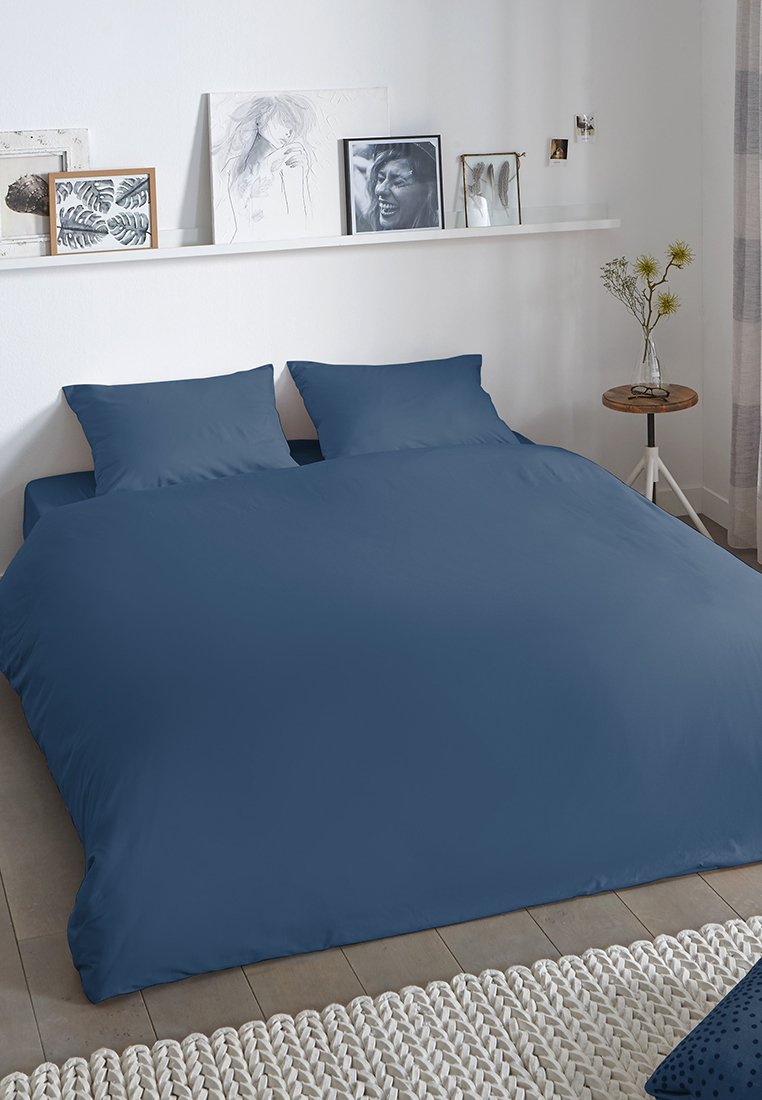 Donkerblauw dekbedovertrekset met twee bijpassende kussenslopen, gladde textuur, eenvoudig ontwerp, geplaatst op een bed met een geweven tapijt in de buurt.