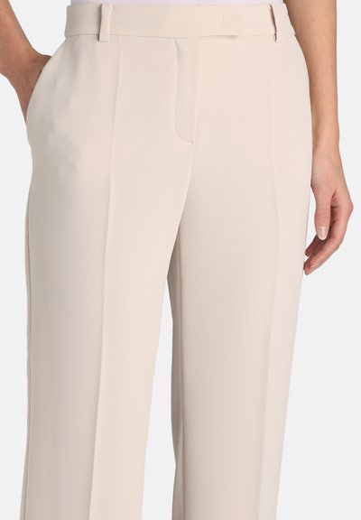 Pantalon beige plissé en tissu lisse, doté de poches latérales et d'une taille cintrée, offrant une silhouette raffinée et longue jusqu'aux chevilles.