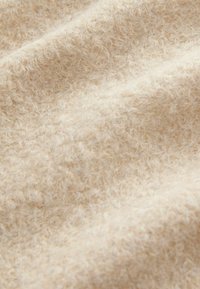 Tissu beige texturé avec une surface douce et duveteuse, exhibant une couleur chaude et naturelle et une apparence invitante et cocooning.