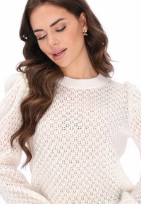 Kötött, krémszínű pulóver texturált, nyitott szövésmintával, pöttyös ujjakkal és gyöngy díszítéssel a vállakon.
