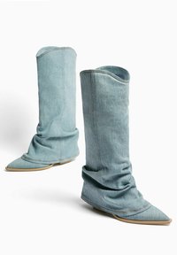 Denim Stiefeletten mit einem lässigen Design, spitzer Zehenpartie, hellblauer Farbe und sichtbaren Nähten. Flache, beige Sohle.