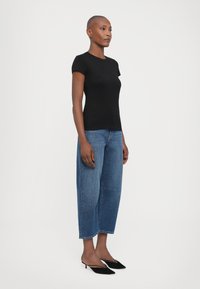 Black fitted t-shirt with short sleeves paired with light blue wide-leg jeans and black slingback heels, displayed against a white background.