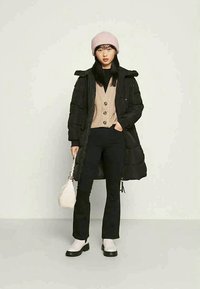 Casaco puffer preto, suéter bege com botões, calças pretas ajustadas, botins brancos, gorro de malha rosa e uma pequena bolsa branca.