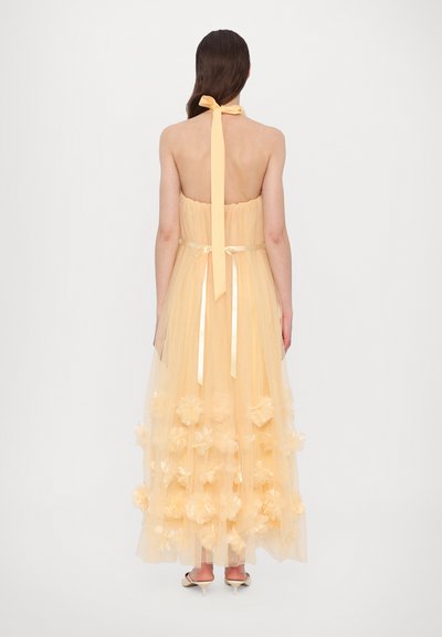 Halterneck maxi-jurk in zachtgele tule, met een aansluitende corsage, een strik aan de achterkant en florale applicaties aan de zoom. Soepele textuur.